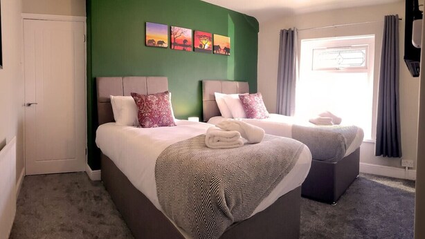 A double room with two beds, a green accent wall, artwork, and a window with curtains. - 4 Bed • Parking • Near M4 • Ideal for Workers (Aberavon)
