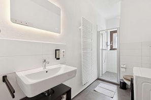 Une salle de bain moderne avec un lavabo blanc, un miroir et une cabine de douche en verre.