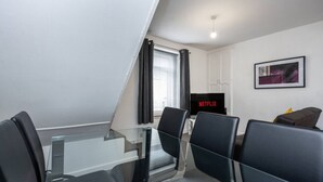 A modern living room with a glass table, black chairs, a flat-screen TV, and a framed picture on the wall. - King•En-suite Flat•Kitchen•Quiet Near Shops & Bus (Swansea)