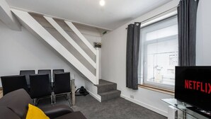 A modern living room with a staircase, a sofa, a TV, and a window with curtains. - King•En-suite Flat•Kitchen•Quiet Near Shops & Bus (Swansea)