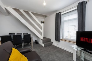A modern living room with a staircase, a sofa, a TV, and a window with curtains. - King•En-suite Flat•Kitchen•Quiet Near Shops & Bus (Swansea)