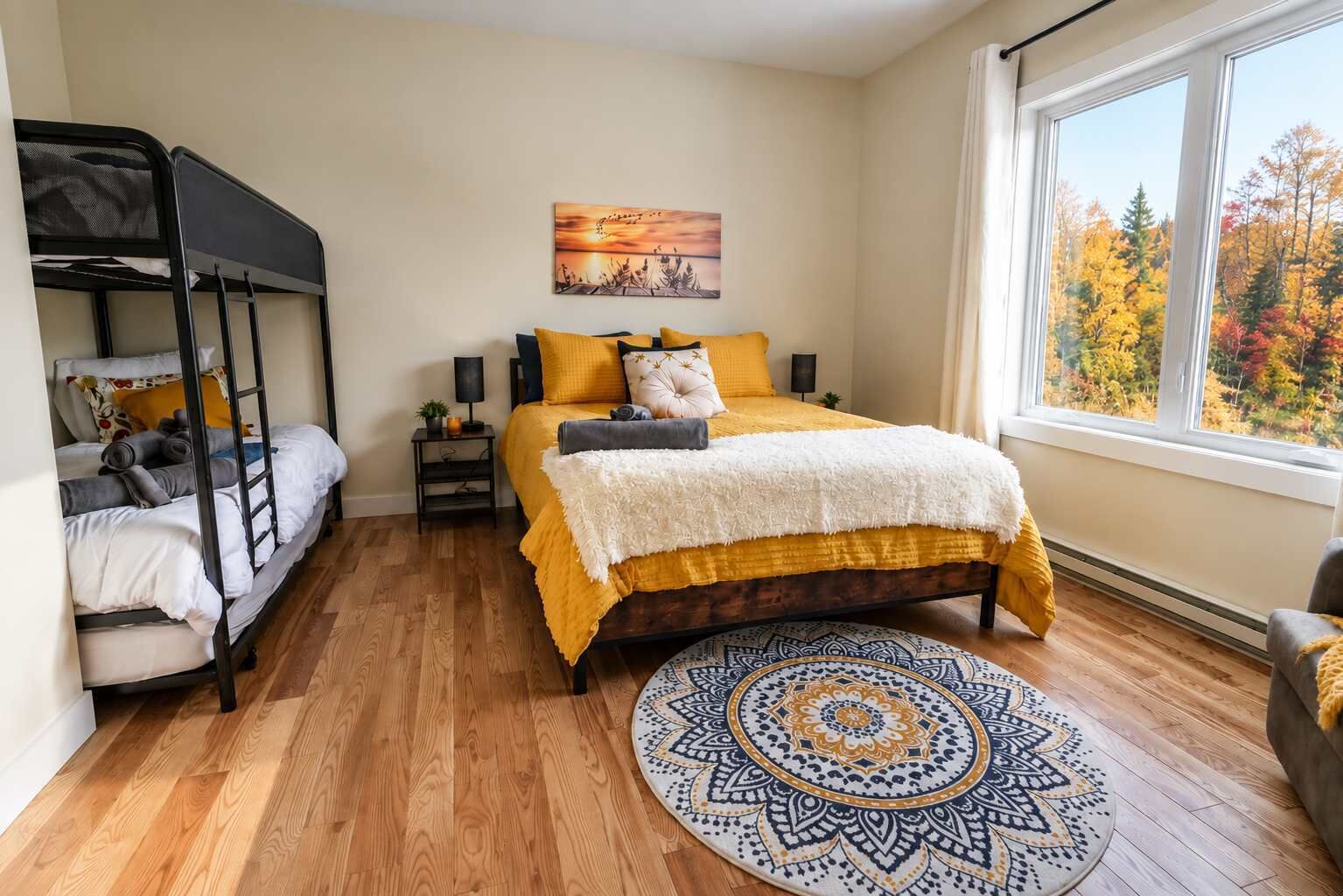 A room with a bunk bed, a single bed with a yellow bedspread, a round patterned rug, a nightstand with a lamp, and a window with a view of autumn trees.
