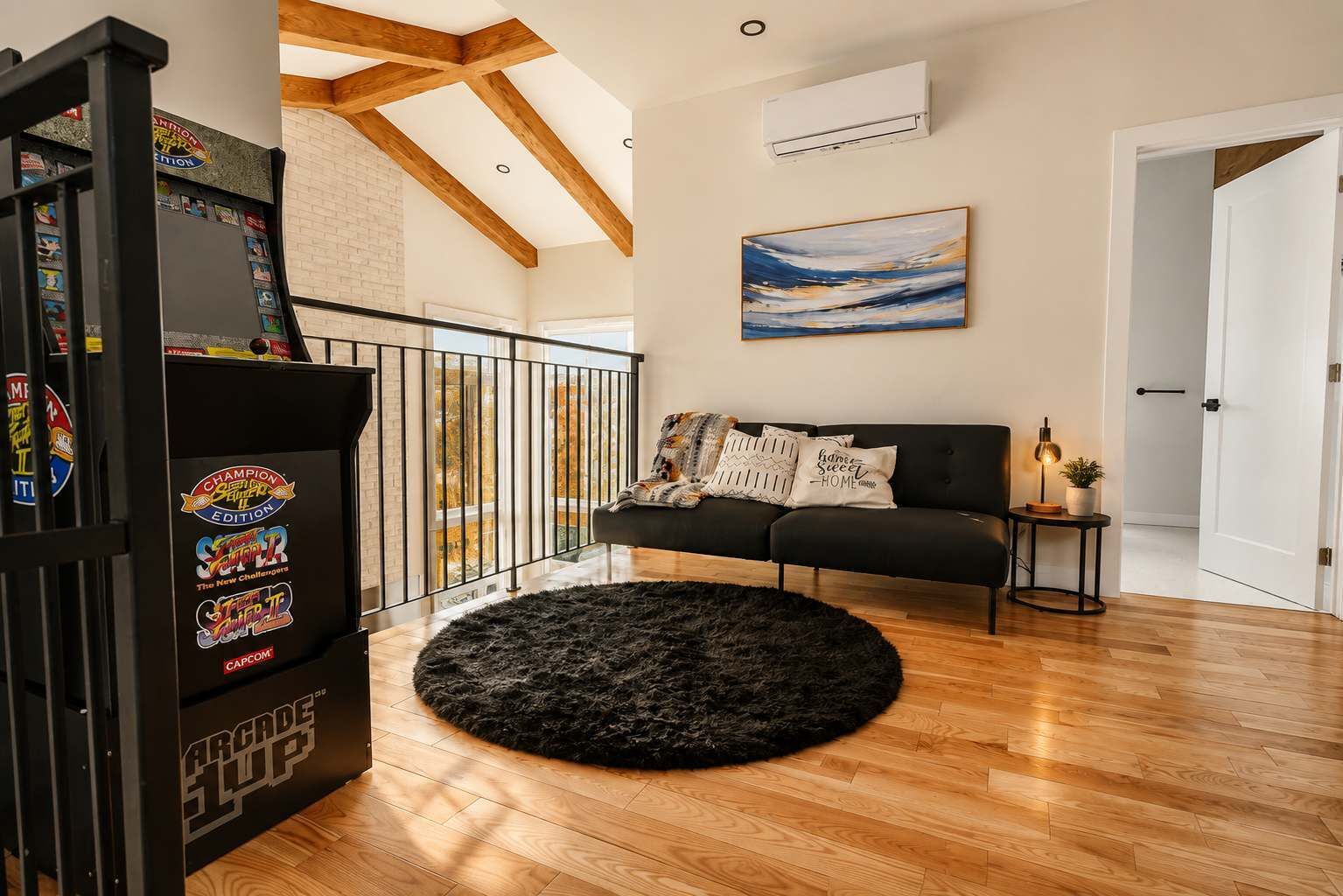 Una sala de estar con un sofá negro, un tapete mullido de color negro, un cuadro en la pared y una consola de videojuegos.