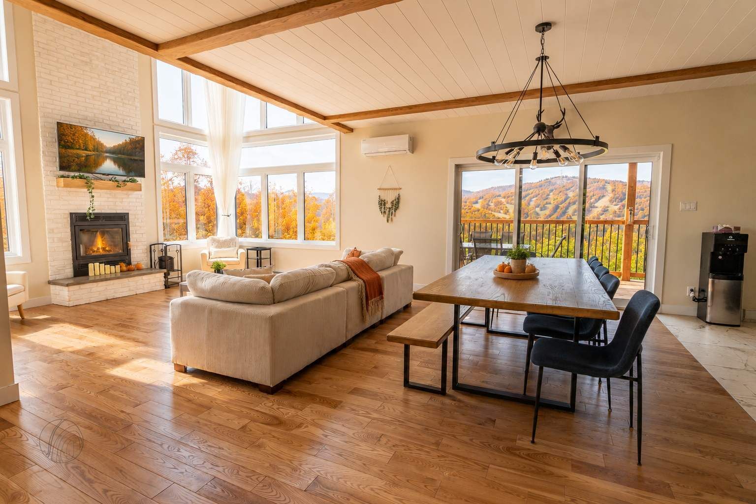 Ein geräumiges Wohnzimmer mit Kamin, einer großen Couch, einem Esstisch mit Stühlen und Blick auf herbstliche Laubfärbung durch große Fenster.