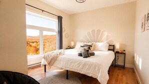 Ein Schlafzimmer mit großem Fenster, einem Bett mit weißer Bettwäsche, einem runden Teppich und einem Nachttisch mit Lampe.