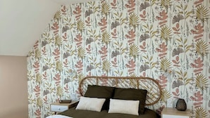 Un dormitorio con cama, mesitas de noche, lámpara colgante y papel tapiz con motivos florales.