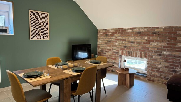 Un comedor con una mesa de madera, sillas, un televisor y una pared de ladrillo.