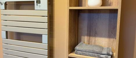 A modern bathroom with a towel rack, a wooden shelf with a vase, and a woven basket.