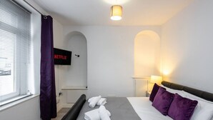 Habitación de hotel con cama, televisor, lámpara y ventana con cortinas.