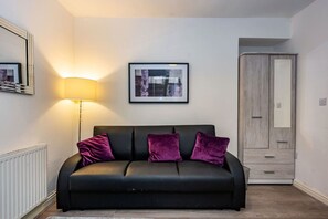 A modern living room with a black sofa, purple cushions, a framed picture on the wall, a standing lamp, and a wardrobe. - En-suite Flat • Kitchen • Quiet Near Shops & Bus (Swansea)