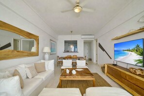 A spacious living room with a white sofa, a wooden coffee table, a dining area with a table and chairs, a large flat-screen TV, and a ceiling fan. - ®{3BR~Hemingway~Retreat}@JuanDolio+WalktoBeach+GYM (Juan Dolio)