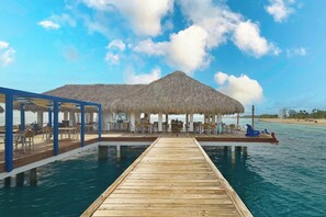 A wooden deck leading to a thatched-roof structure with outdoor seating, overlooking a body of water. - ®{3BR~Hemingway~Retreat}@JuanDolio+WalktoBeach+GYM (Juan Dolio)