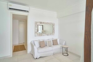 Une pièce blanche comprenant un canapé, une petite table ronde et un miroir avec un cadre décoratif.