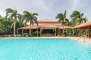 Une piscine avec des chaises longues, un pavillon abrité et des palmiers.