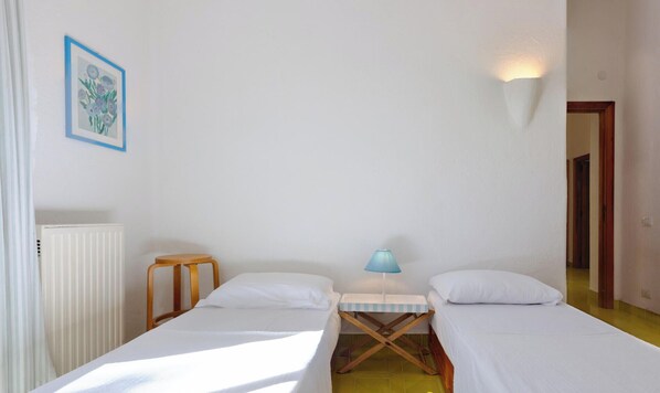 Ein Zimmer mit zwei Betten, einem kleinen Tisch mit Lampe, einem Heizkörper und einem gerahmten Bild an der Wand.