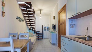 Eine moderne Küche mit Einbauherd, ein Essbereich mit Holztisch und -stühlen sowie eine Treppe, die zu einer weiteren Ebene führt.