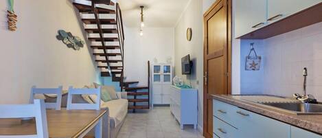 Una cocina moderna con estufa integrada, un comedor con mesa y sillas de madera, y una escalera que lleva a otro nivel.