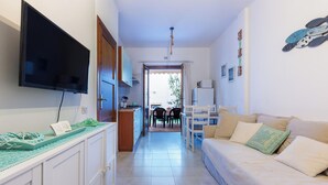 Ein schmaler Flur führt zu einem Essbereich mit Tisch und Stühlen, einem Sofa, einem an der Wand befestigten Fernseher und einer Deckenleuchte.