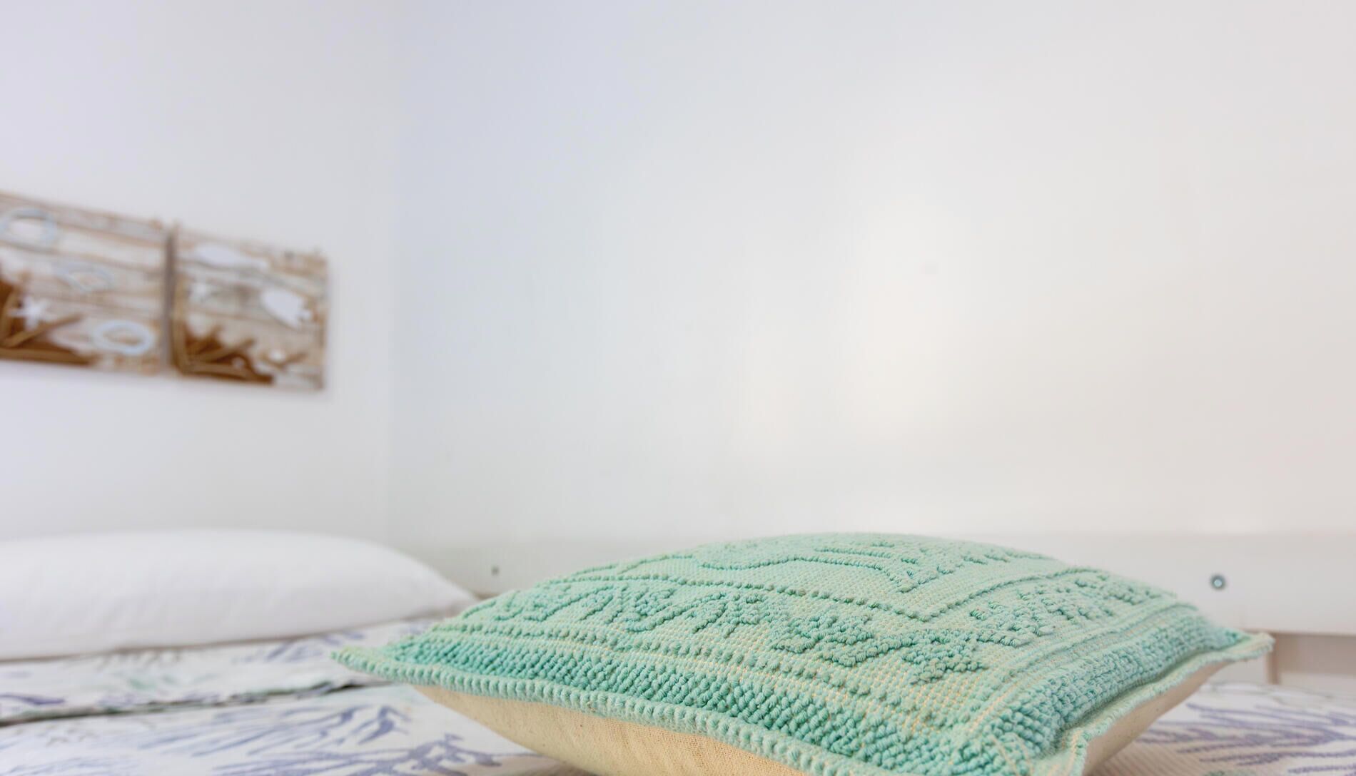 Un lit avec un coussin tricoté de couleur vert clair, un coussin blanc et une couverture à motifs.