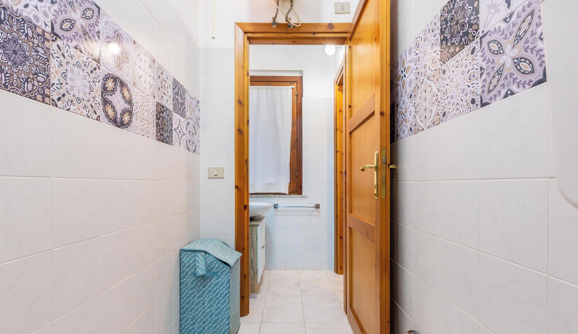A narrow hallway with patterned tiles, a wooden door, and a small sink with a towel.