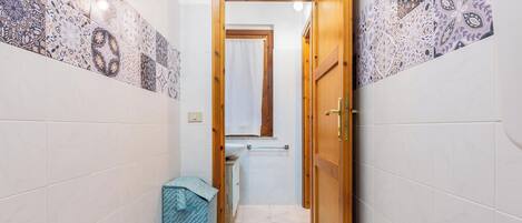 A narrow hallway with patterned tiles, a wooden door, and a small sink with a towel.