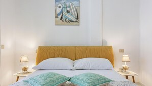 Ein Bett mit weißen Kissen und einer grünen Decke, zwei Nachttischlampen sowie ein Bild von Surfbrettern an der Wand.