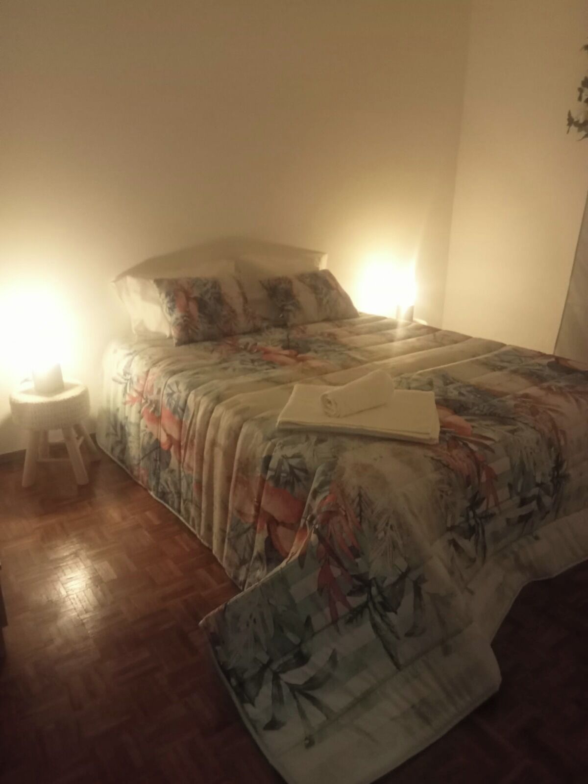 A bedroom with a bed, a nightstand, and a small stool.