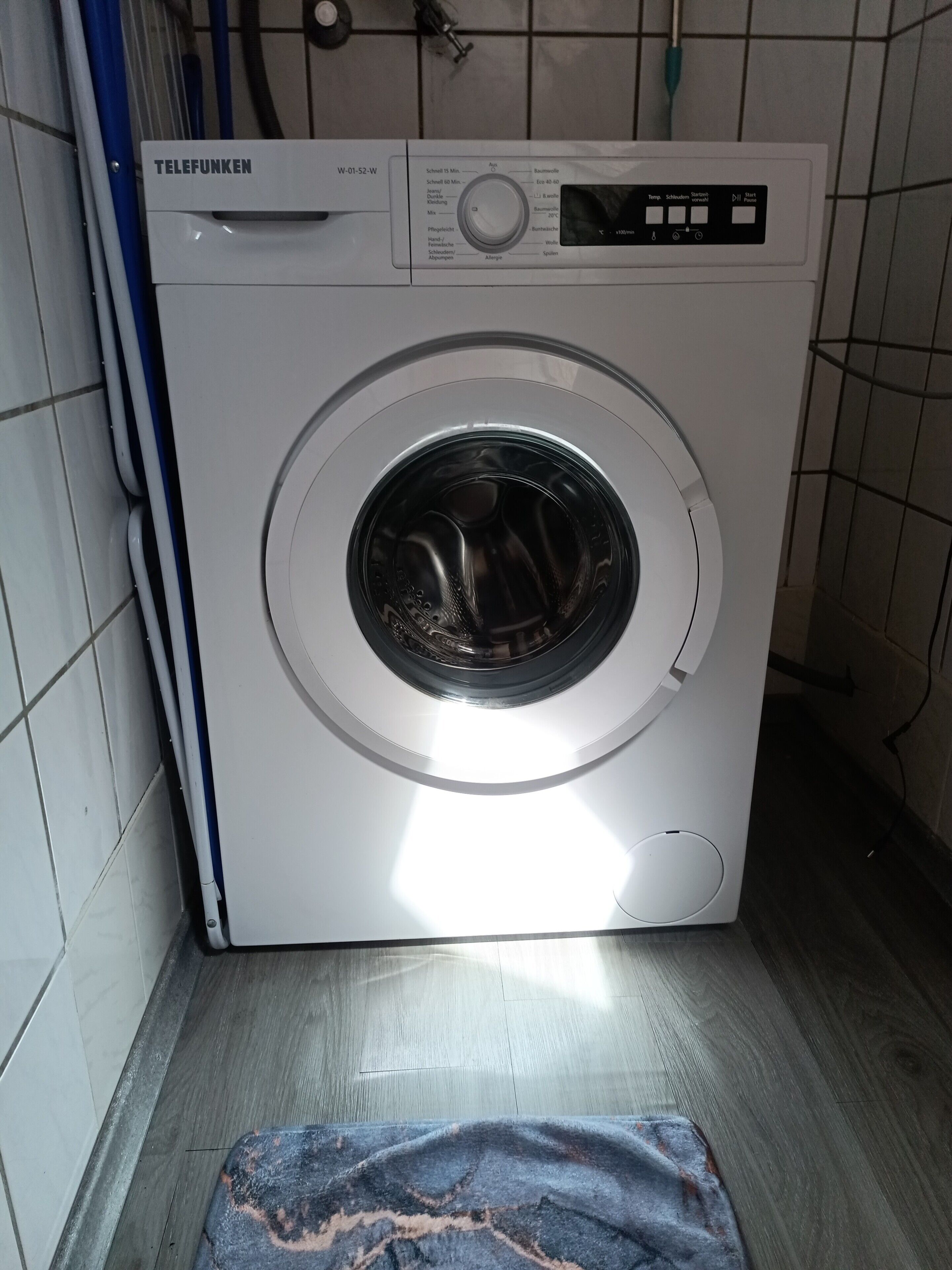 Een wasmachine met voorlaadopening in een wasserij met betegelde wanden en een houten vloer.