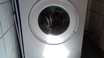 Een wasmachine met voorlaadopening in een wasserij met betegelde wanden en een houten vloer.