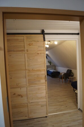 Puerta corredera de madera que da a una habitación con una cama, una silla y una mesita.