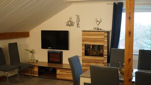 Ein modernes Wohnzimmer mit Flachbildfernseher, Kamin und Essbereich mit Stühlen und Tisch.