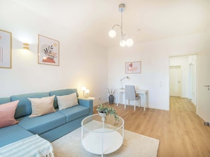 A modern living room with a blue sofa, a glass coffee table, and a desk with a chair. - Lemon3: 1 Bedroom Apartment with Balcony (Karlsruhe)