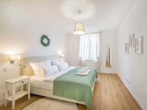 A neatly arranged bedroom with a bed, bedside tables, a hanging light, a window with curtains, and a wall-mounted mirror. - Lemon3: 1 Bedroom Apartment with Balcony (Karlsruhe)