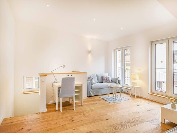 A bright room with a desk, chair, sofa, and a small table with a lamp.