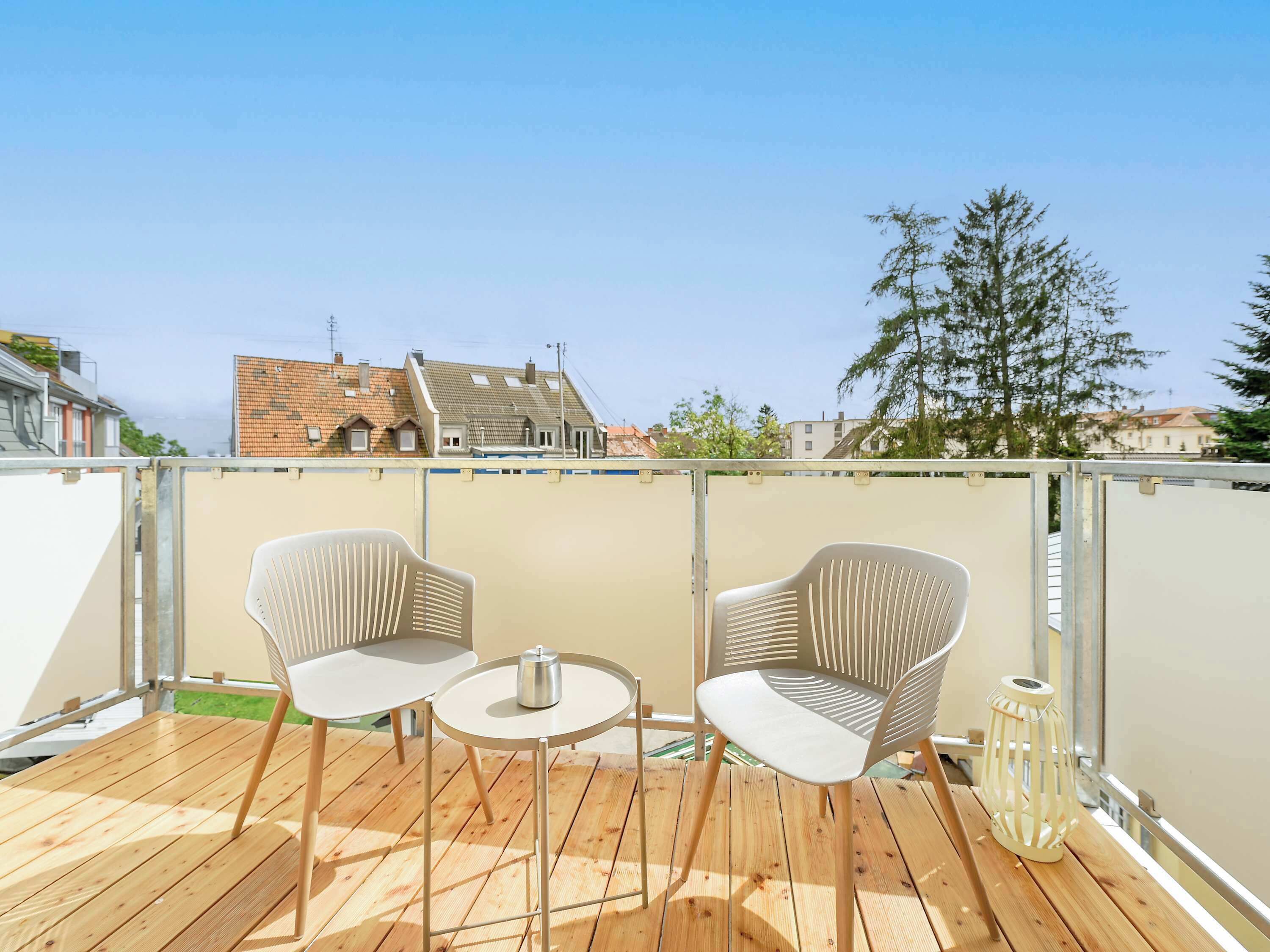 A wooden deck with two white chairs and a small table, overlooking a residential area with houses and trees.