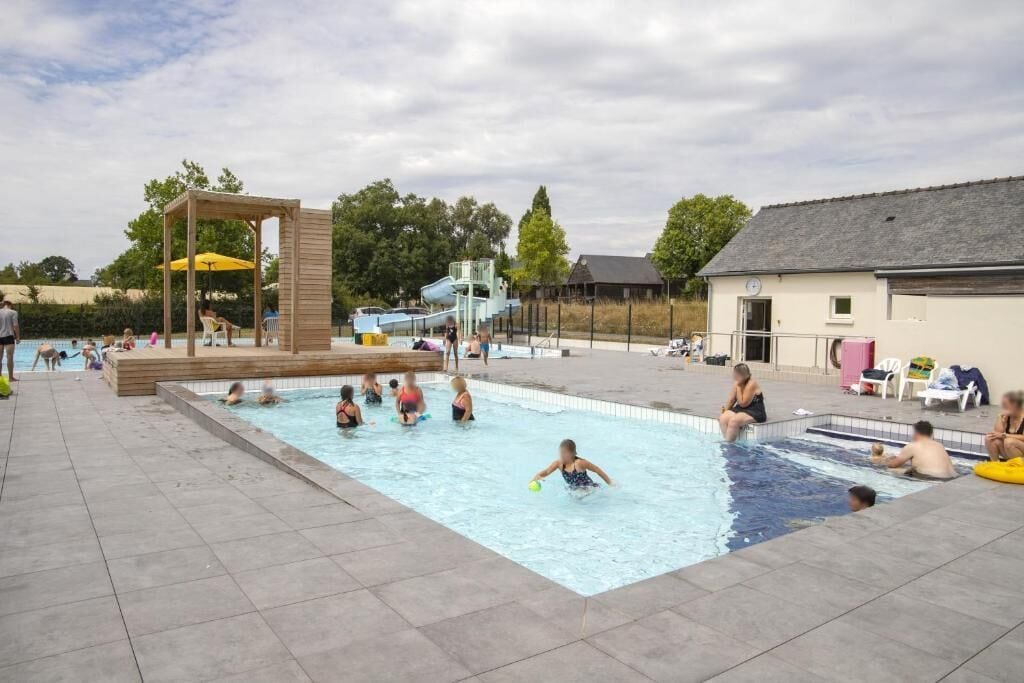 Zona de piscina con estructura de madera, tobogán y un edificio al fondo.