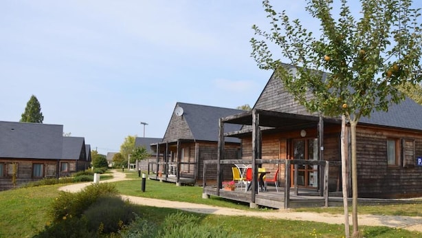 A row of wooden cabins with a covered porch, a pathway, and a tree in the foreground. - Les Lodges de Sainte-Suzanne (Sainte-Suzanne-and-Chammes)