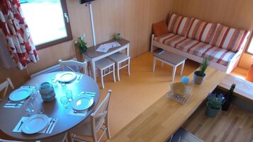 Un espacio habitable compacto con una mesa de comedor para cuatro personas, un sofá, una pequeña cocina y una ventana con cortinas.