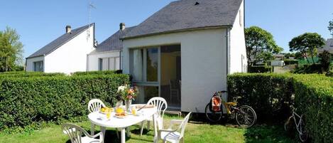 A house with a white exterior, a grey roof, and a small patio with a table and chairs.