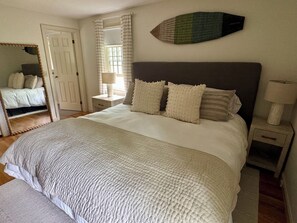 A bedroom with a bed, bedside tables, a mirror, and a window with curtains.
