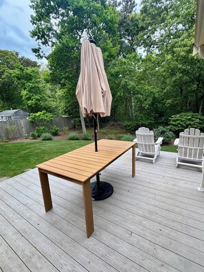 A wooden deck with a table and chairs, surrounded by a grassy yard and trees.