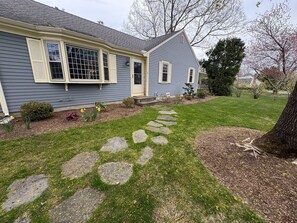 A house with a stone pathway leading to the front door, surrounded by a well-maintained lawn and small shrubs.