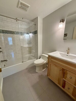 Et badeværelse med en brusekabine i glas, toilet, vask med spejl og træskabe.
