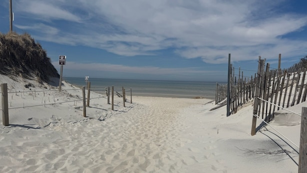 En sandstrand med et træhegn og et skilt, der står 'KEEP OFF DUNES'.