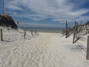 Ein sandiger Strand mit einer Holzlattenverkleidung und einem Schild mit der Aufschrift 'KEEP OFF DUNES'.
