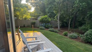 En terrasse med to hvide Adirondack-stole, et træhegn og en velplejet græsplæne med forskellige planter.
