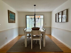 A dining area with a wooden table, chairs, a rug, a chandelier, and a window with a view.