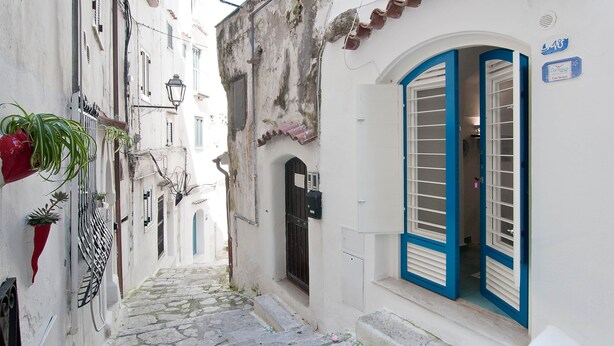 Une rue étroite avec un bâtiment blanc, une porte bleue et une petite enseigne.