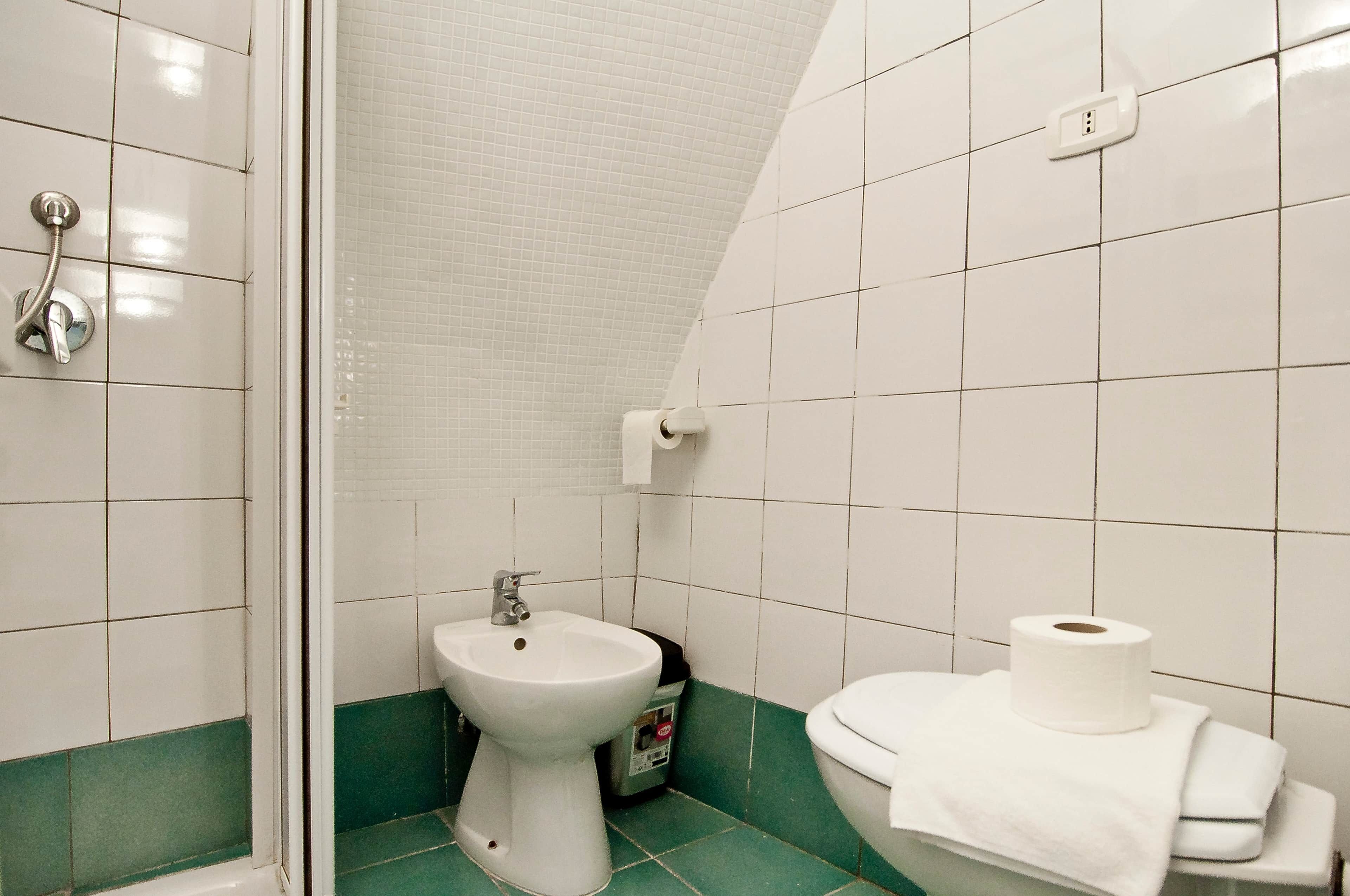 Une salle de bain avec douche, bidet, toilettes et carrelage vert au sol.