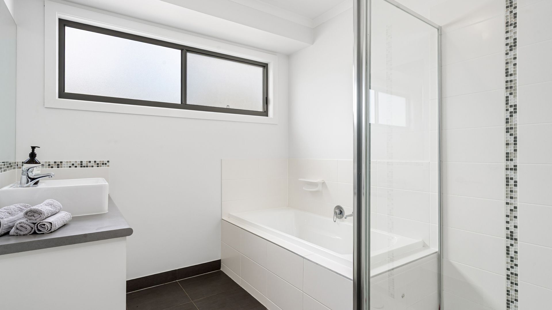 Une salle de bain moderne avec un lavabo blanc, un miroir, une fenêtre au-dessus du lavabo, une baignoire et un espace douche.